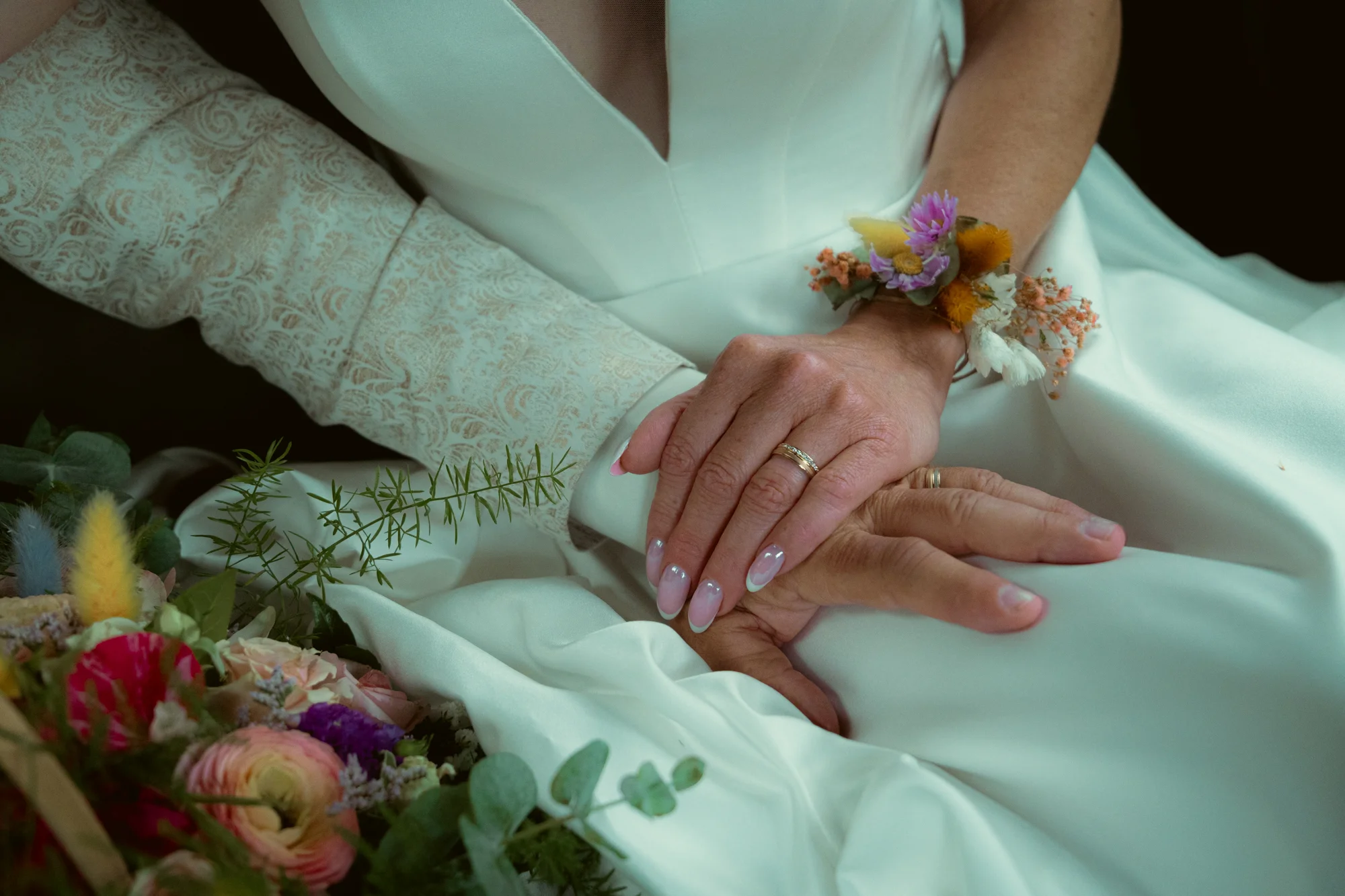 Mains des mariés avec alliances et bracelet de fleurs, bouquet coloré