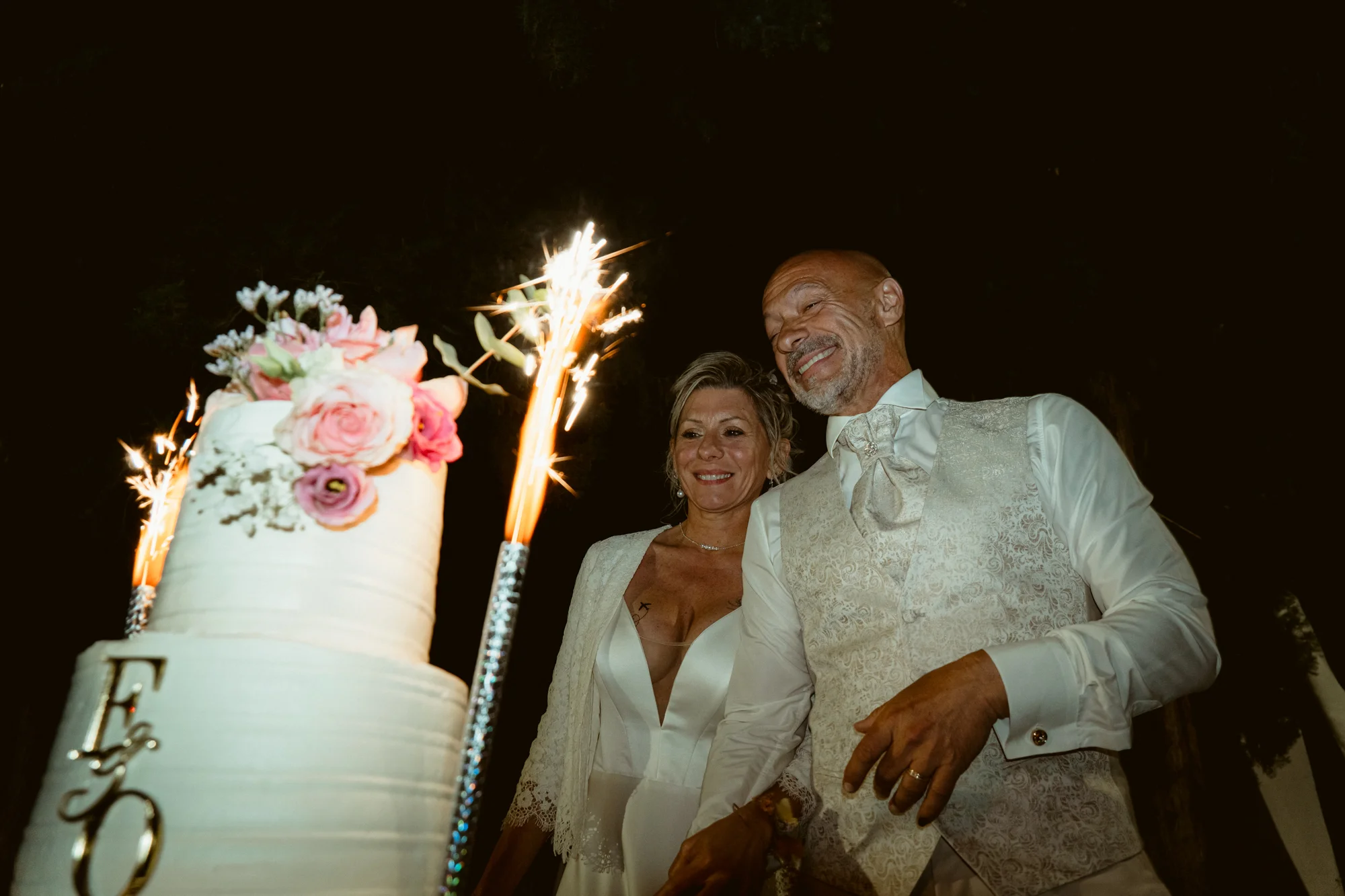 Découpe du gâteau de mariage avec cierges magiques, mariés souriants la nuit